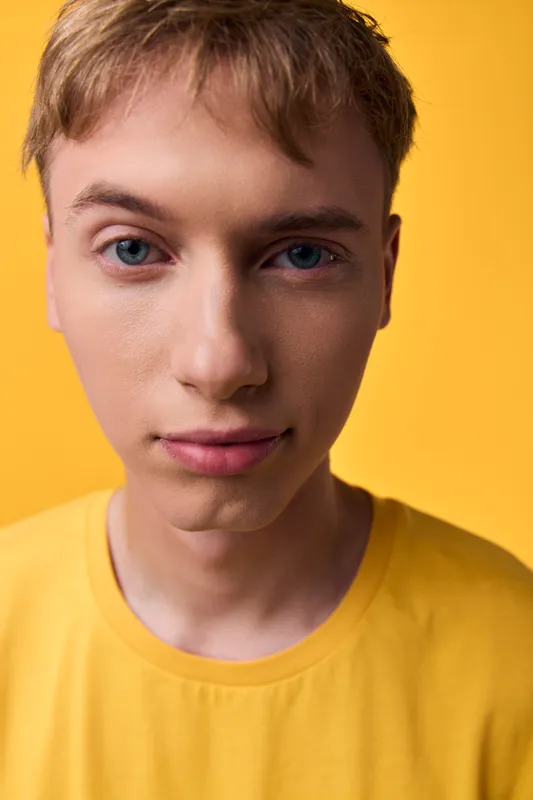 Closeup of a man with short hair and calm expression, wearing a yellow shirt against a warm yellow background, clear skin and even studio lighting, presenting a simple, clean, modern look