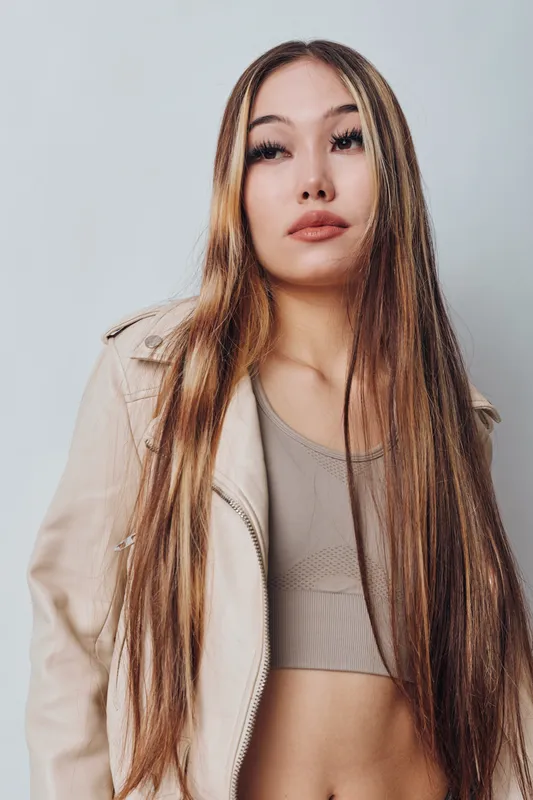 Young woman with long straight hair wearing casual beige jacket and crop top posing isolated in studio for fashion and beauty portrait, lifestyle and style concept.