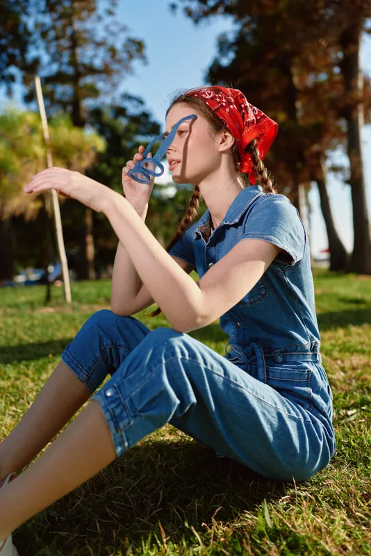 lifestyle woman in modern boho-western denim street style with red bandana under golden sunlight, enjoying outdoor moment captured in warm film color tones.