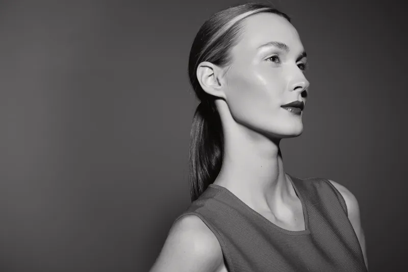 Profile of a young Caucasian woman with pale skin and slicked-back hair looks confidently to the side against a plain background. Concept of elegance and minimalism.