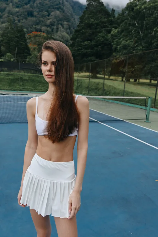 Young female tennis player in sporty attire, showcasing confidence and athleticism on a tennis court surrounded by greenery, vibrant colors emphasize energy and summer vibe