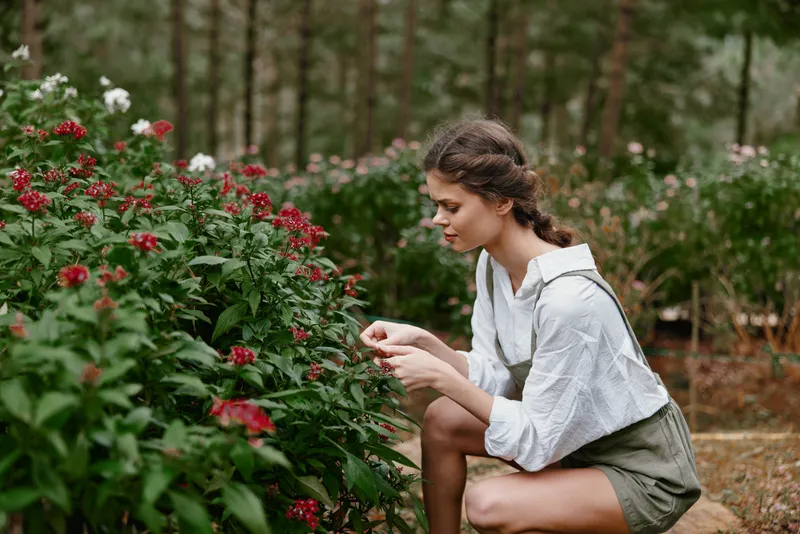 Young woman picking flowers in a lush garden, wearing a casual outfit, showcasing emotions of joy and tranquility amidst vibrant greenery, perfect for nature concepts