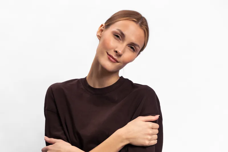 Young woman with light skin and brown hair wears dark sweater, posing with crossed arms and slight smile on white background. Concept of confidence, calmness, and casual style.