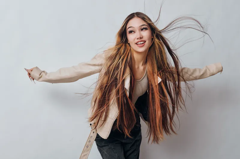 Young woman with long hair dancing and smiling in casual outfit against plain background. Movement, joy, beauty and fashion with happy gesture and lifestyle concept.