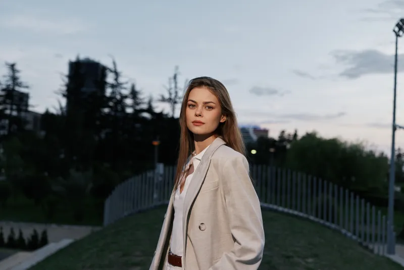 Confident woman in a business suit standing outdoors, showcasing professionalism against a scenic urban background during twilight.