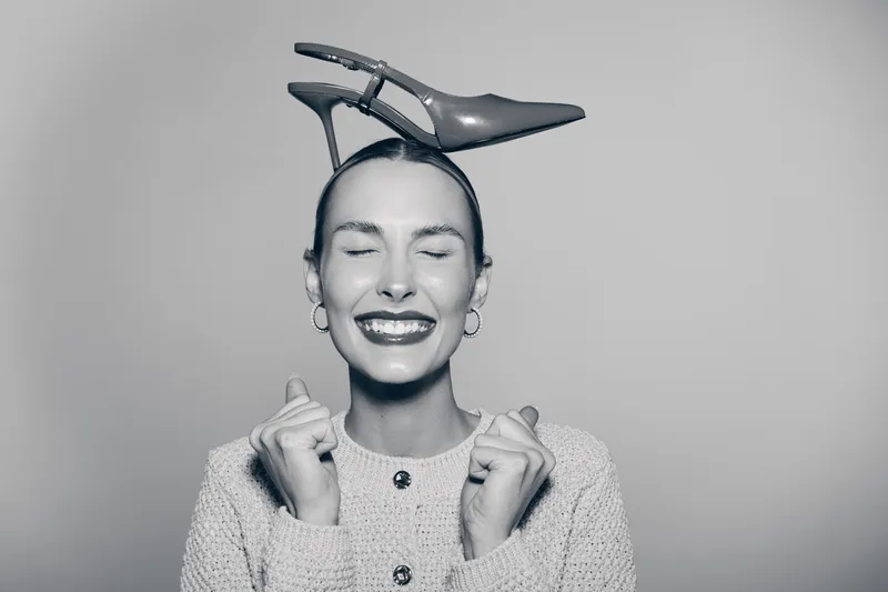 Happy Caucasian woman with fair skin smiling with closed eyes wearing shoe on head in creative concept.