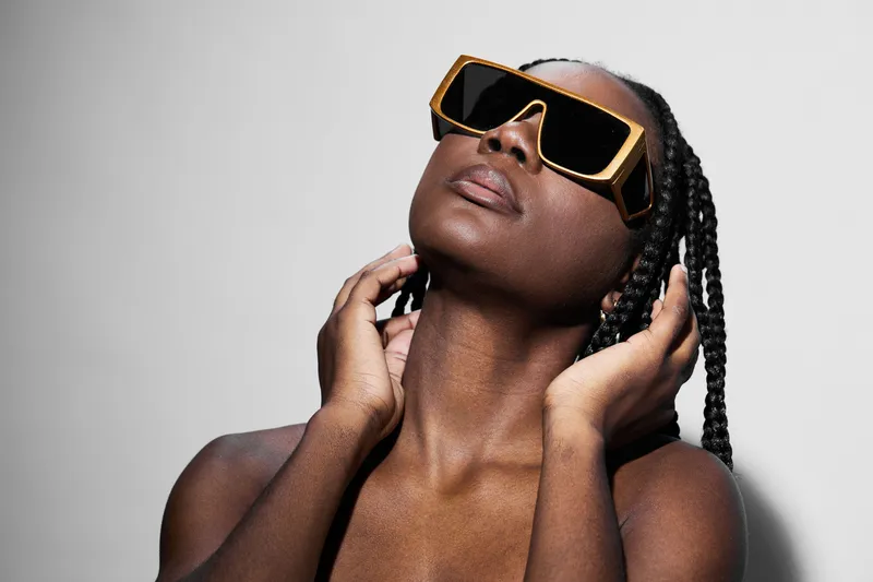 Stylish black woman in oversized sunglasses showcasing confidence, capturing modern fashion and beauty aesthetics against a minimalist backdrop