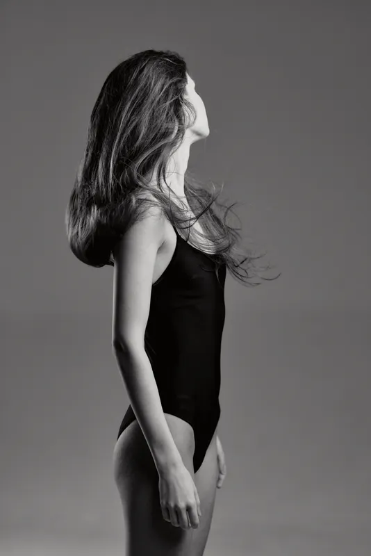 Black and white portrait of a woman with long hair in a black leotard, expressing graceful movement and elegance.