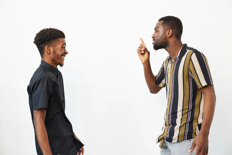 Two black men having an intense conversation, with one listening attentively while the other gestures passionately. The dynamic captures a moment of connection.