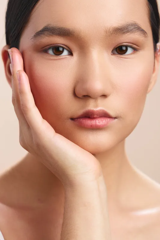 Asian woman in a clean studio presents a calm, poised expression, with smooth skin and subtle makeup, creating a serene beauty portrait under soft, flattering light.