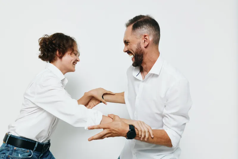 A professional man in business attire shares a moment of emotion on an isolated colored backdrop, showing confidence and warmth as he engages in a friendly handshake and maintains open posture.