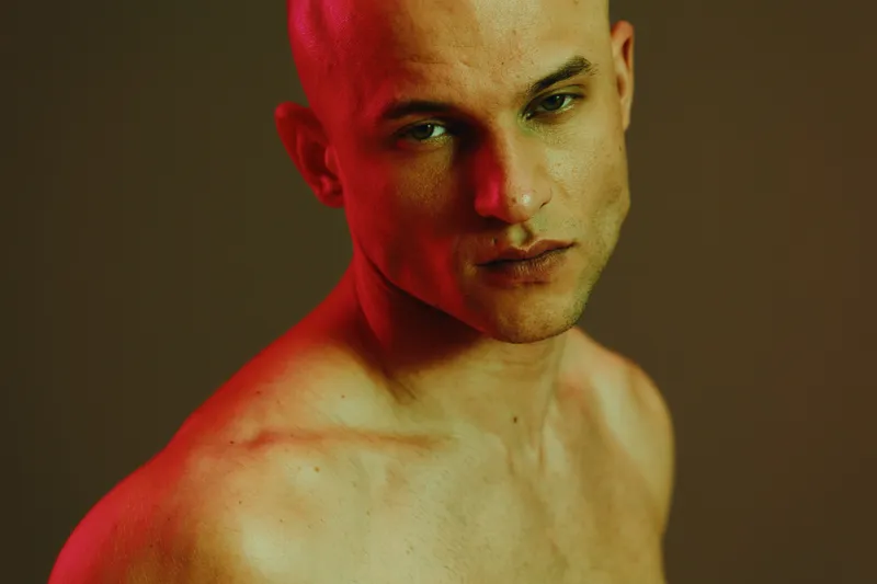 Striking portrait of a man with a bold expression, showcasing strong features against a vibrant background. The image captures the essence of modern masculinity.