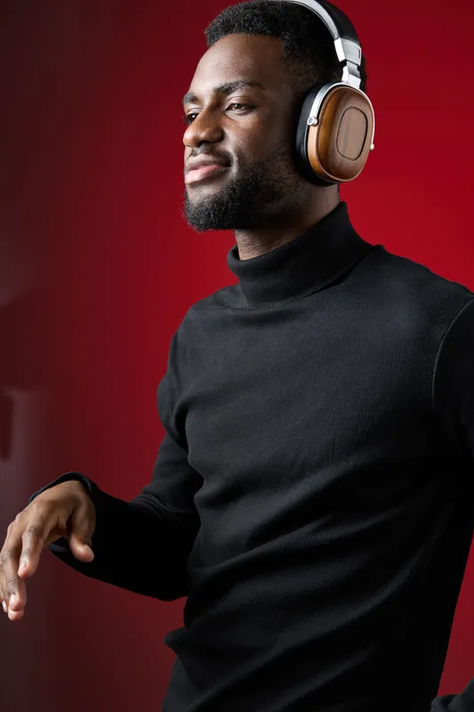 Young Black man enjoying music with headphones against a vibrant red background, expressing joy and relaxation in a stylish black turtleneck