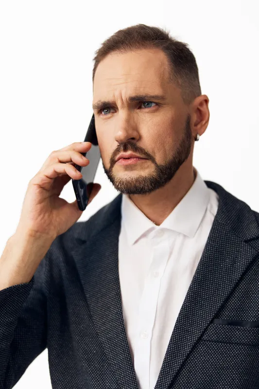 A professional man on a business call, displaying focused determination and thoughtful emotion, stands against a clean isolated colored background.