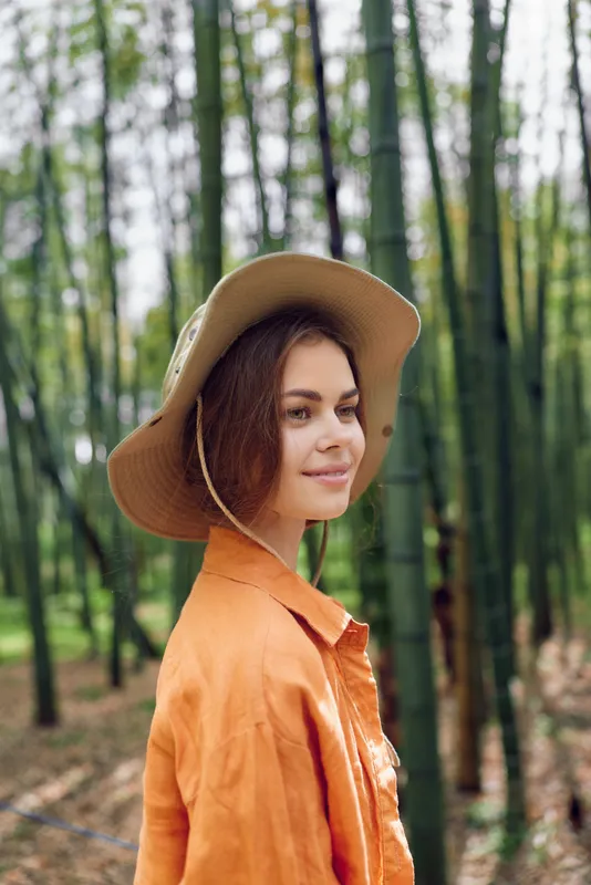 woman portrait bamboo hat smile nature forest travel outdoors wearing an orange shirt, relaxed model with serene expression and soft sunlight, profile view for lifestyle, vacation and exploration