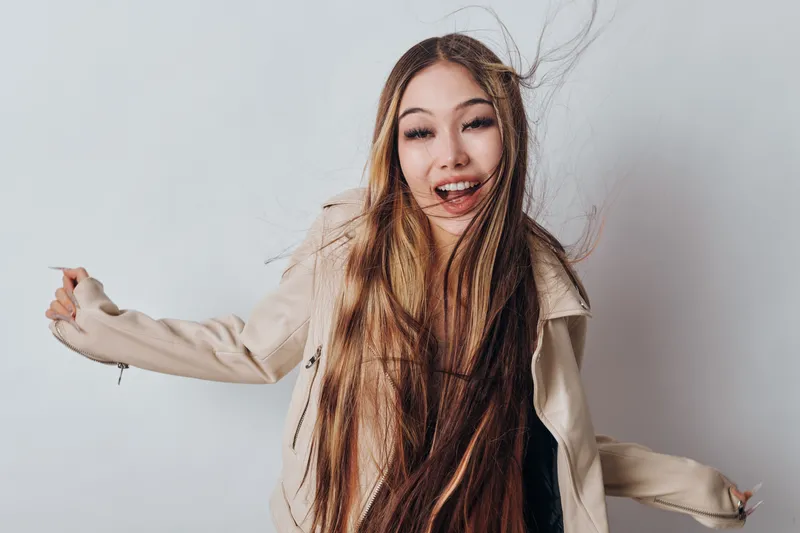 Young woman with long hair in beige jacket dancing and smiling on white background for lifestyle, happiness and casual fashion portrait.