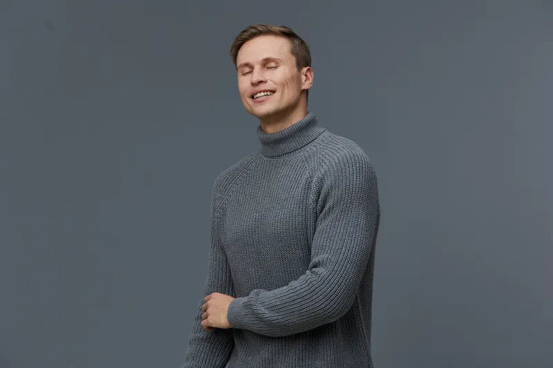 smiling man in gray knitted turtleneck enjoy digital detox close eyes relaxed casual wear plain gray background studio portrait mental health concept