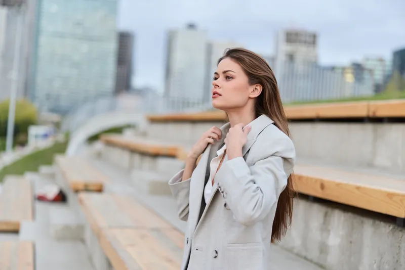 Woman in beige coat outdoors with confident pose and city background in spring urban fashion style