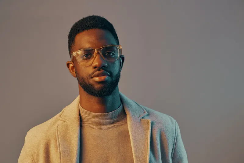 Portrait of a stylish dark skinned man wearing glasses and a light sweater against a soft gradient background, reflecting modern fashion trends and self confidence