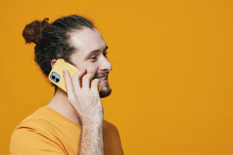 Young smiling man talking on a yellow phone against a vibrant yellow background, showcasing modern lifestyle and communication concepts vividly