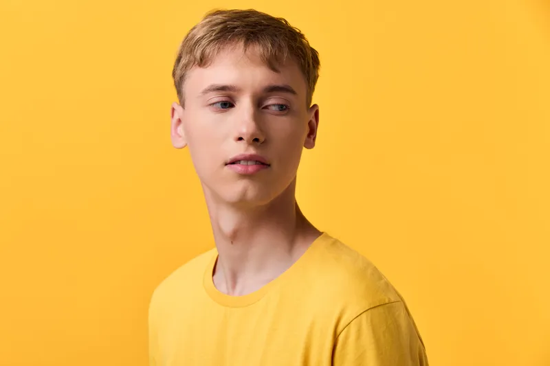 Young man, yellow background, yellow shirt, contemplative expression, studio lighting, minimal color, clean composition, fashion photography style, versatile mood for branding and social media