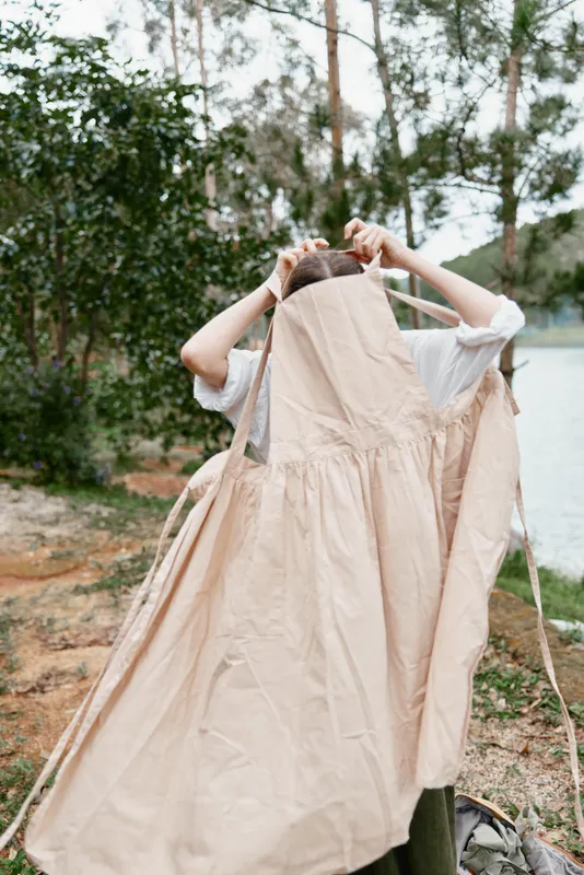 A woman in a natural setting wearing a flowy beige dress, capturing a moment of tranquility by a calm lake surrounded by greenery
