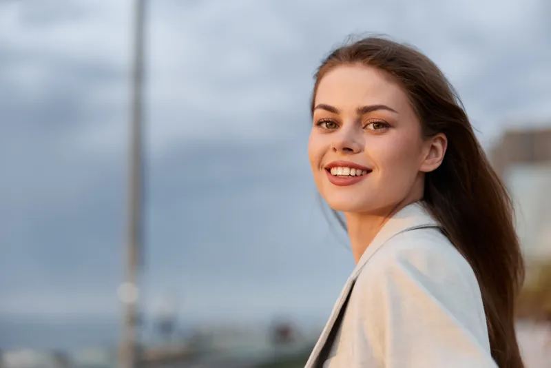 Young woman smiling confidently outdoors in light gray jacket with natural background and soft lighting, casual fashion style, spring season emotion