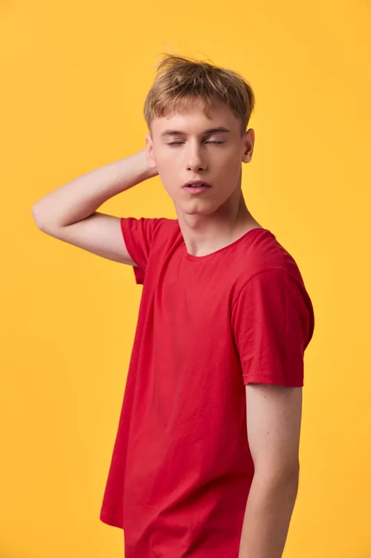 Young man in a red shirt strikes a casual pose against a bold yellow background, conveying relaxed style, contemporary fashion and a thoughtful mood for lifestyle photography