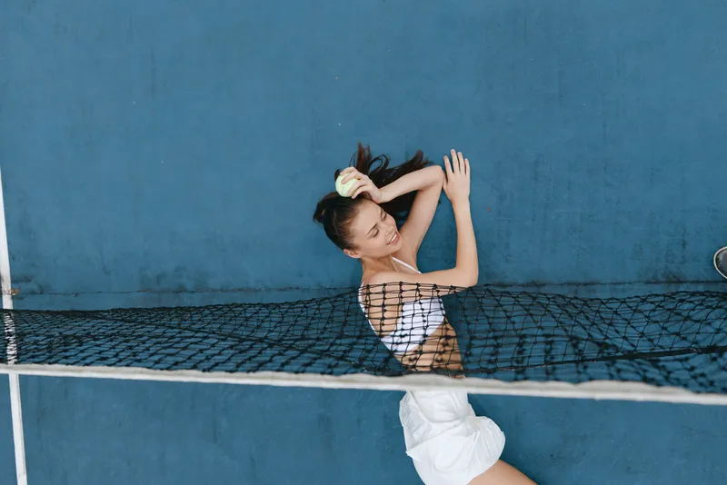 Young female athlete relaxing with a tennis ball on a blue court, showcasing a sense of calm and focus, ideal for sports and wellness themes