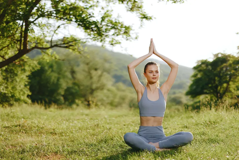 Young woman practicing yoga outdoors in nature, wearing a blue outfit, exuding calmness and serenity in a lush green setting