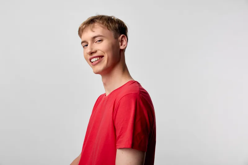 Smiling man in a red shirt in a clean studio, casual and confident, expressing happiness through relaxed pose and upbeat energy, ideal for marketing, fashion, or lifestyle branding