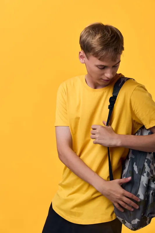 Boy in a yellow shirt with a camouflage backpack against a bright yellow background, ready for school, preparing for learning, casual style and youthful energy in everyday education.