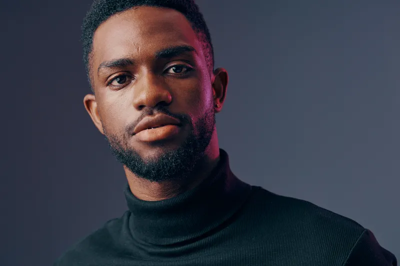 Portrait of a confident African man in a black turtleneck against a dark background, showcasing emotions of self assurance and style
