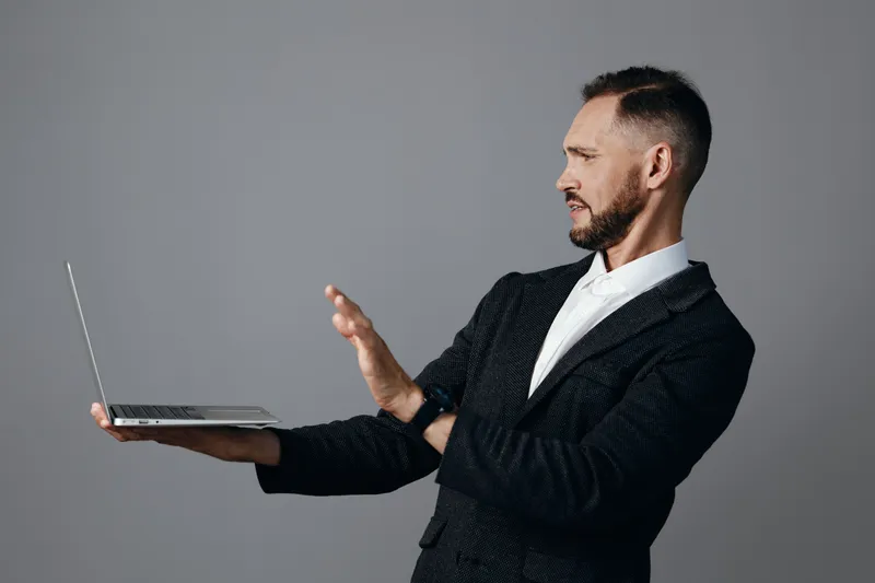 A professional man in business attire presents a laptop against an isolated colored background, exuding confidence, calm focus, and a modern executive vibe.