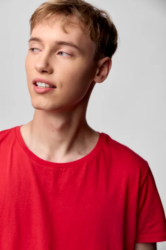 Boy in a red shirt with casual style, thoughtful gaze, studio lighting highlighting smooth skin and modern youth fashion, clean background, ideal for lifestyle or fashion stock imagery