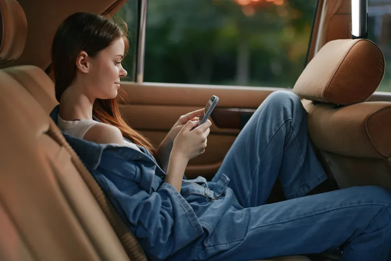 Young woman in casual denim outfit texting on phone in a car interior, relaxed and focused, soft lighting, modern style