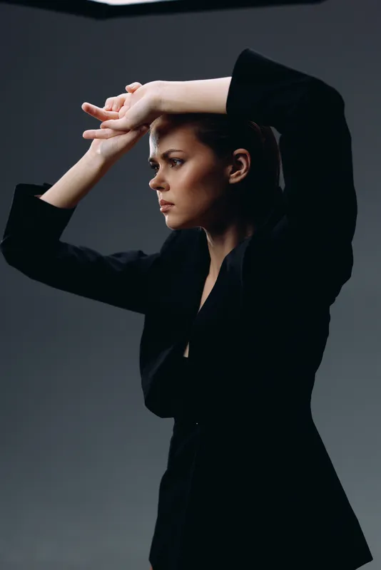 serious woman in black jacket with folded arms looking away in dark studio setting