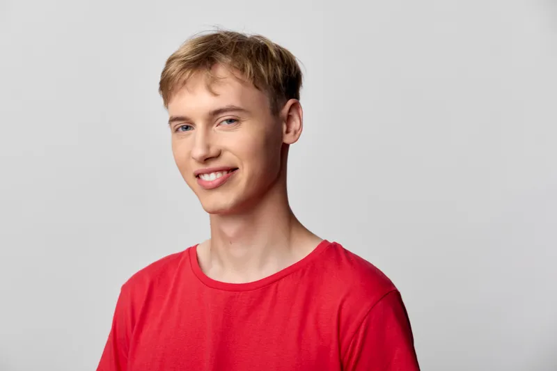 Smiling man wearing a redshirt stands against a neutral studio background, delivering casual confidence and modern lifestyle appeal suitable for fashion, lifestyle, and advertising uses.