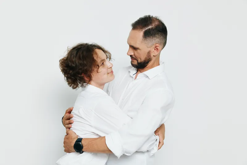 A professional man and partner share a warm embrace against a clean colored background, conveying confidence, teamwork, and emotion in a business setting.
