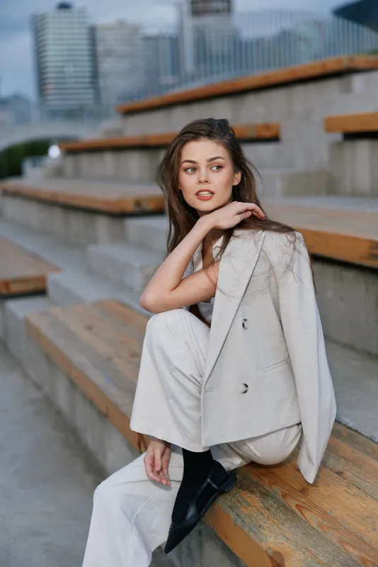 woman sitting on urban stairs wearing beige suit jacket and pants with stylish black shoes in autumn fashion business portrait