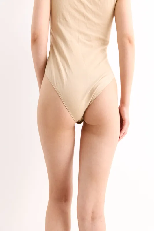 woman wearing beige bodysuit standing with back turned, minimalistic background, natural skin tones, soft lighting, neutral colors