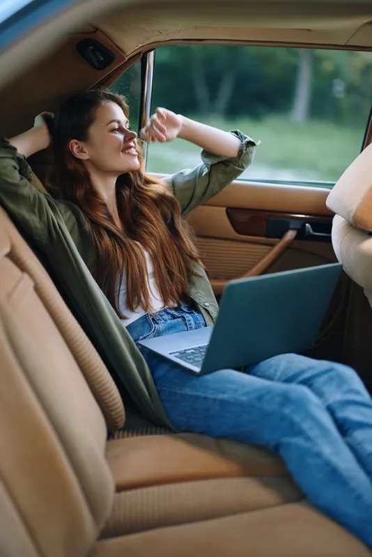Young woman relaxing in car with laptop, enjoying serene moment, evoking joy and creativity in nature-inspired setting.