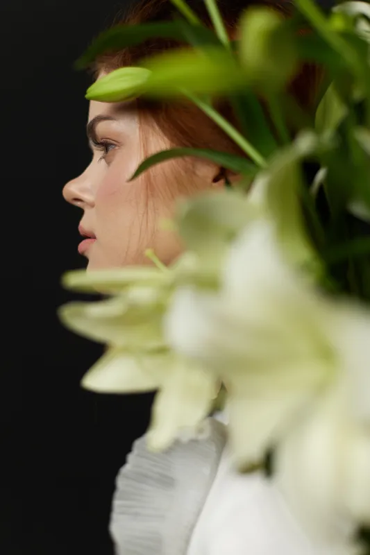 Profile of a young woman surrounded by fresh white flowers on a dark background, conveying natural beauty and serenity in a modern style