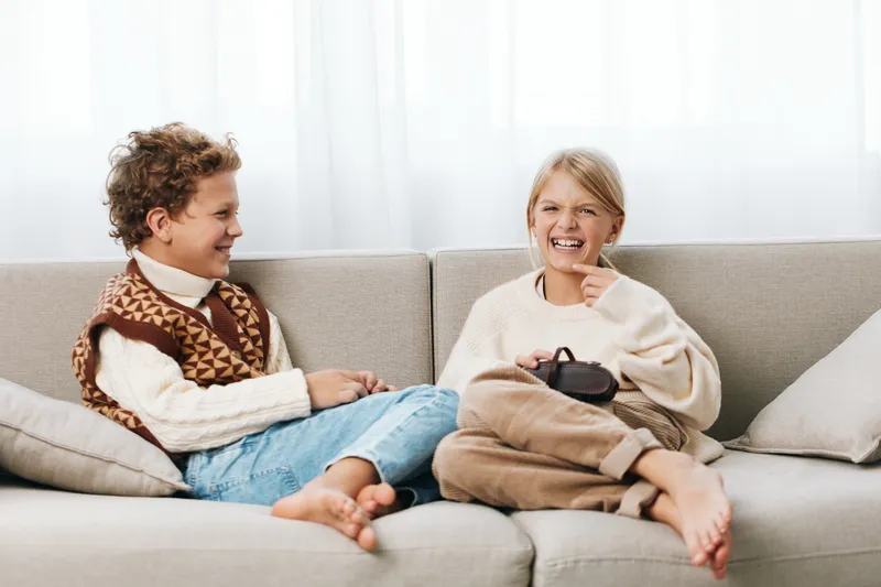 Authentic scene of children at home enjoying playful moments on a cozy sofa, casual attire, genuine smiles, capturing everyday life and a lighthearted school inspired vibe.