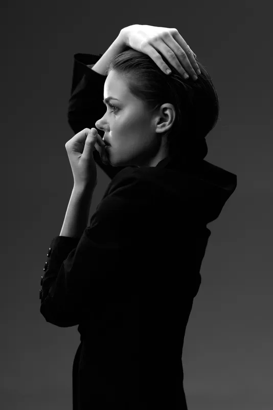 Black and white portrait of a thoughtful woman in a dark outfit with sleek hair and expressive pose