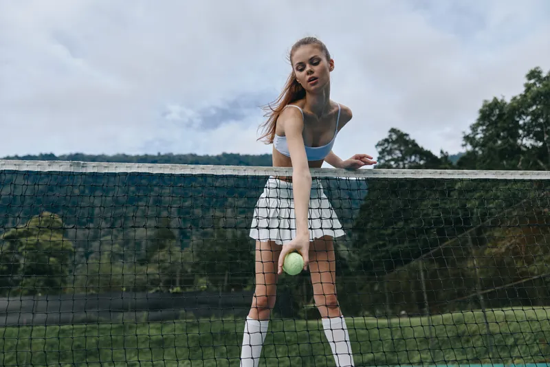 Young female tennis player preparing to serve on a sunny day, dressed in a sporty outfit, exuding confidence and focus in a vibrant outdoor setting