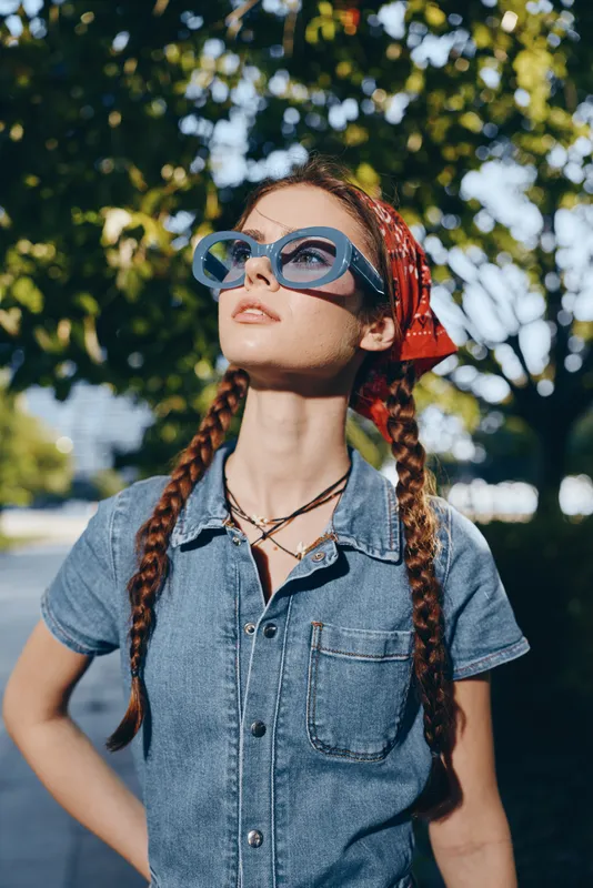 Lifestyle woman in modern boho-western denim street style with red bandana and blue sunglasses, vibrant film color capturing casual summer urban vibe outdoors.