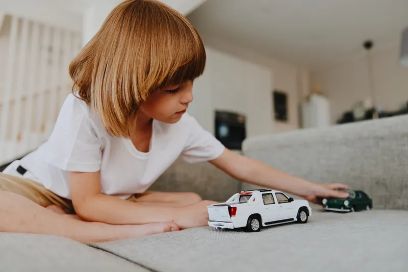 A focused boy playing with toy cars on a cozy sofa in a bright living room, engaging in imaginative play and enjoying his time indoors with vibrant colors.