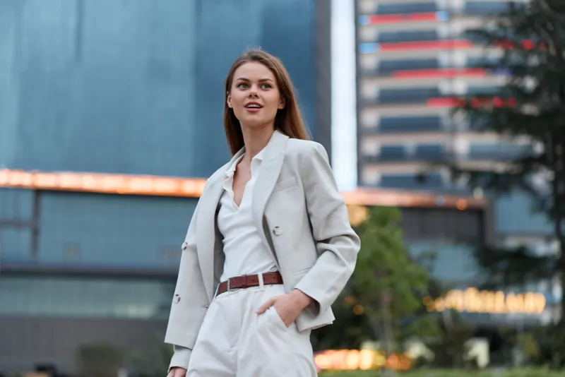 Confident businesswoman in a stylish gray suit standing outside an urban office building, showcasing modern professional fashion and vibrancy.