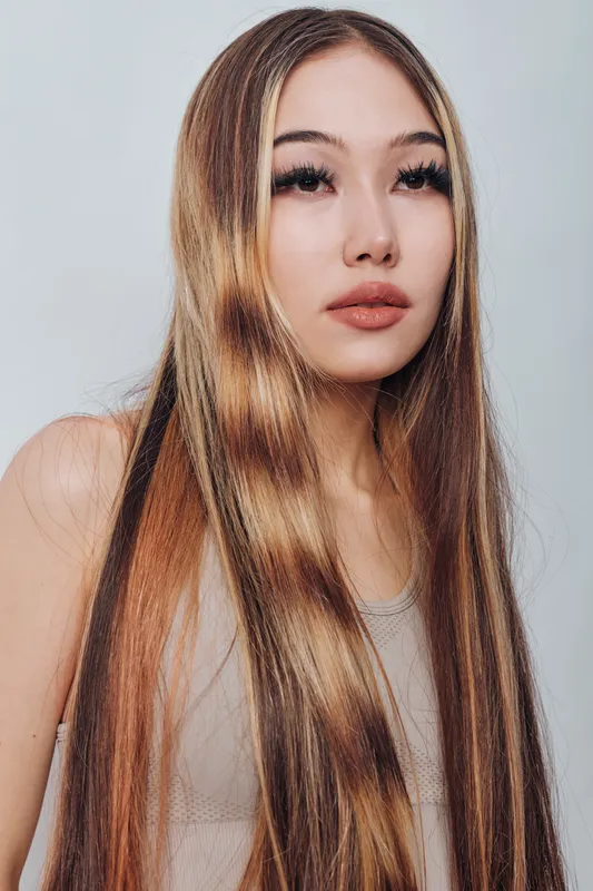 Young woman portrait with long straight hair and natural makeup looking away with calm expression on light background. Beauty, fashion and youth concept with casual style.